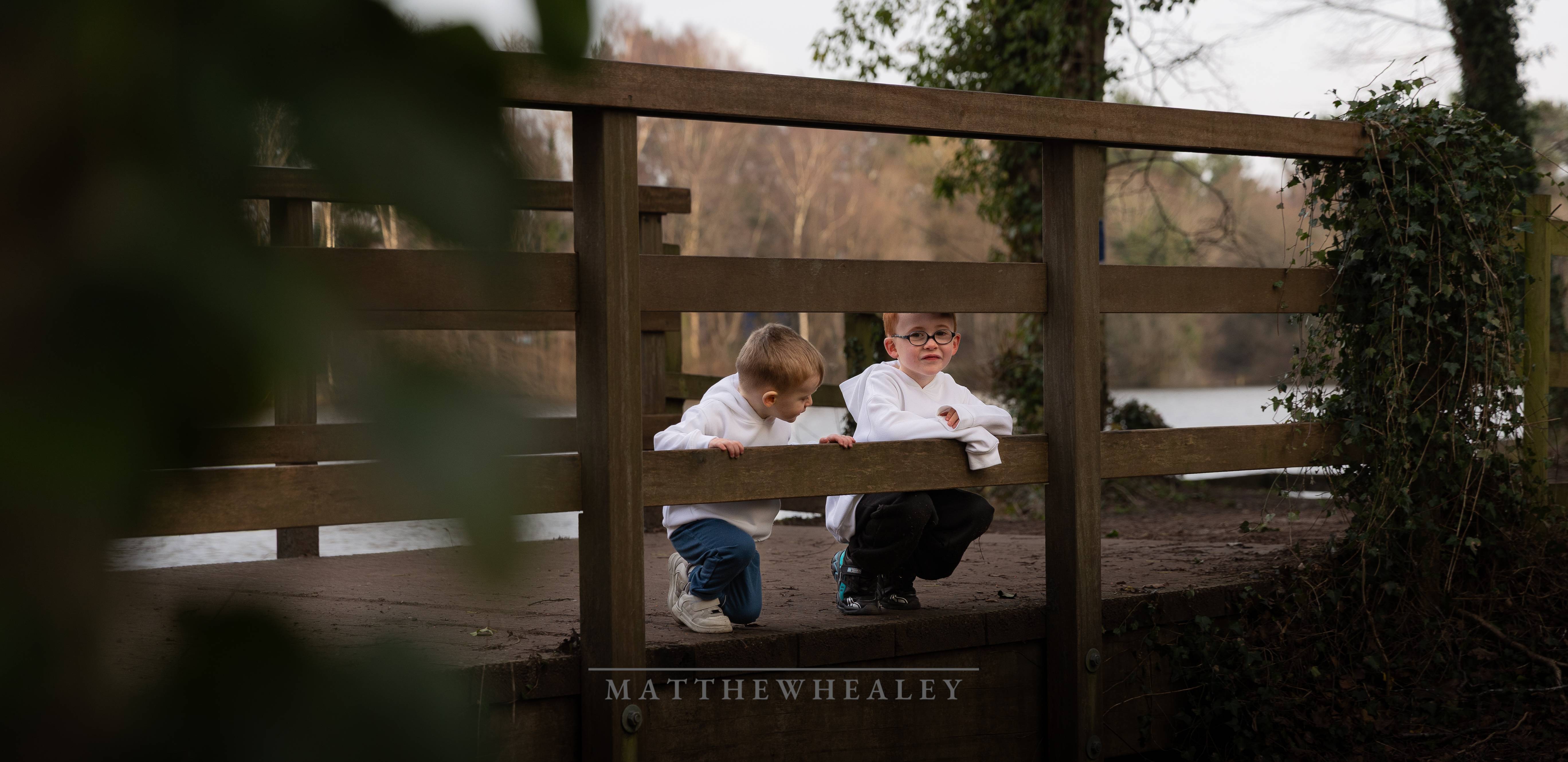 2 boys crouching through a fence, professional photography