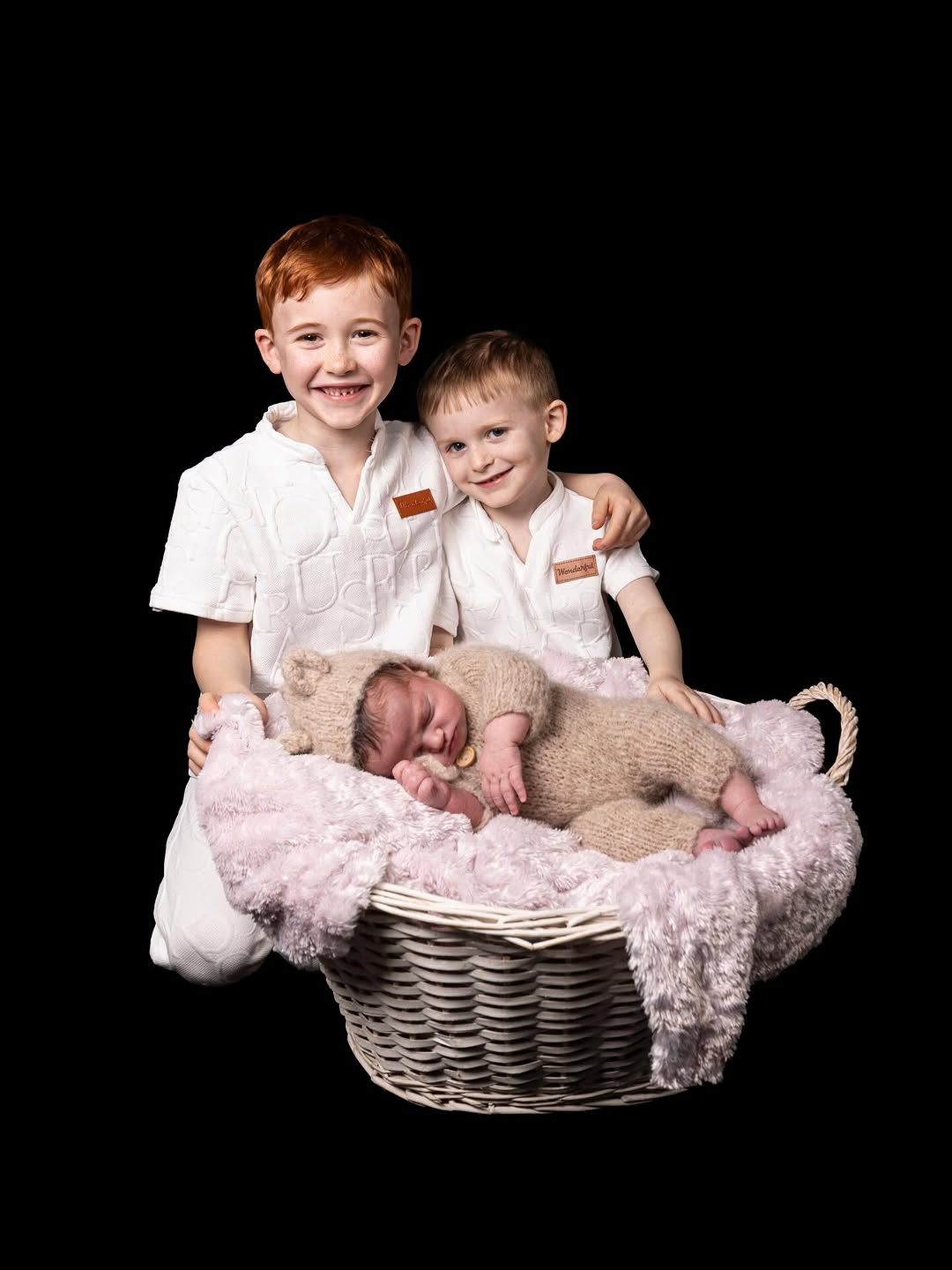 2 boys and a baby in a basket infront of a black backdrop